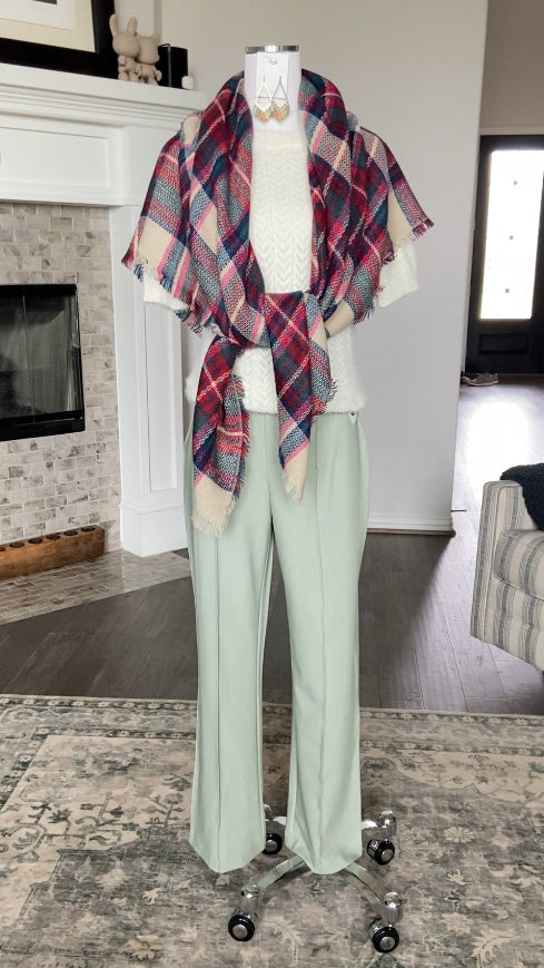 Mannequin wearing the Erica Plaid Oversized Scarf Shawl Blanket in colors cherry, pink, red, teal, blue, and beige by www.thehouseofblondie.com, white sweater, and sage green pants in a room with a fireplace.