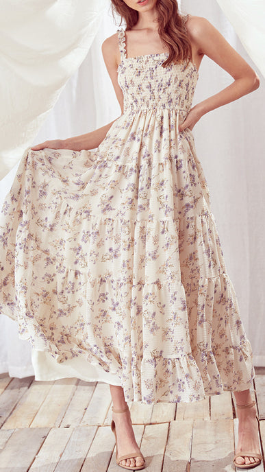 Woman wearing a floral dress on a wooden floor with white curtains in the background
