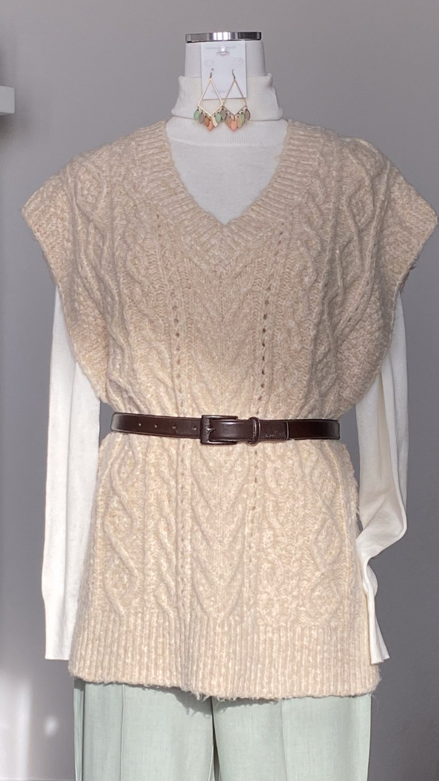 Beige V-neck knitted sweater vest with a brown belt on a mannequin against a gray background