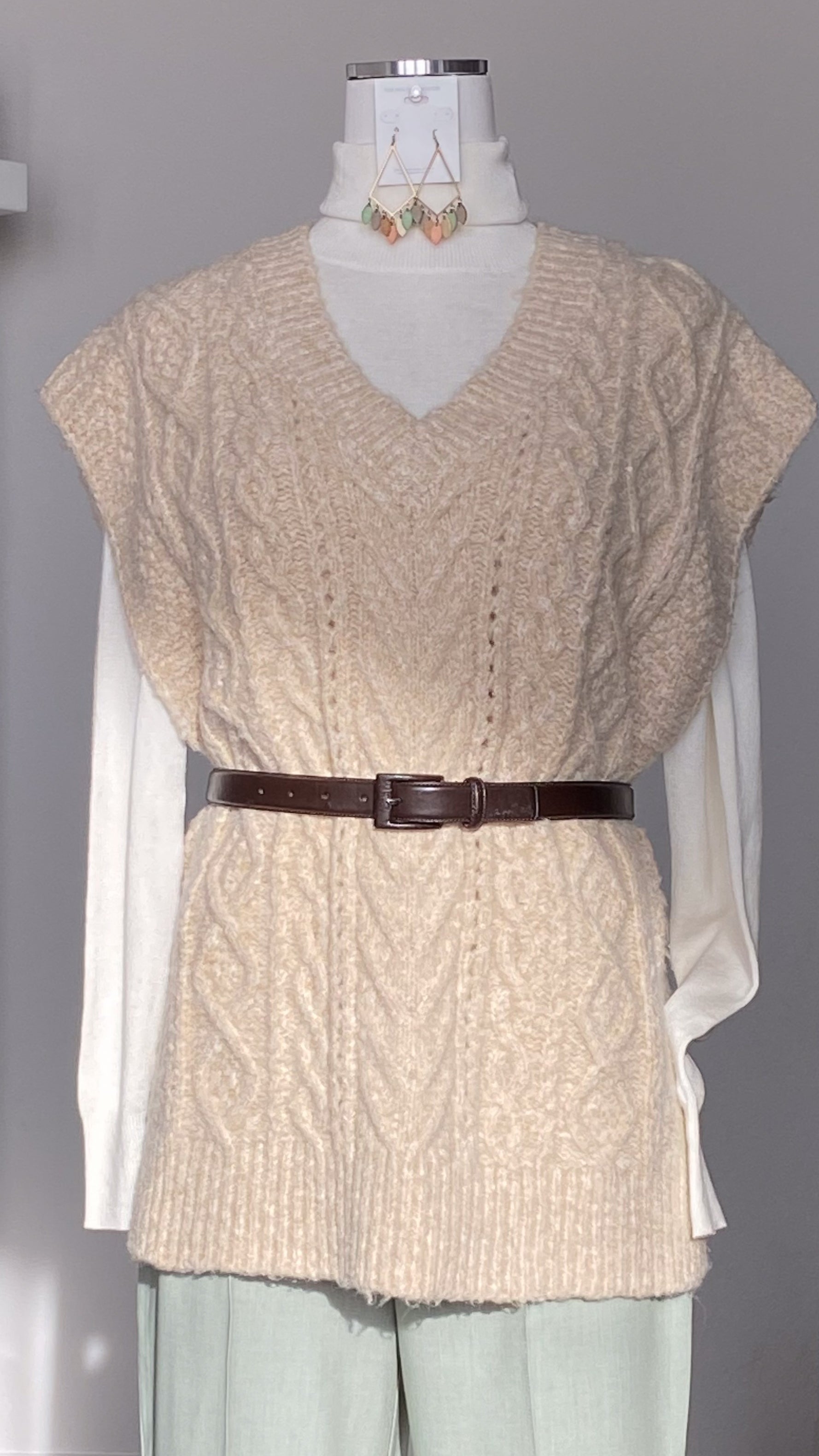 Beige V-neck knitted sweater vest with a brown belt on a mannequin against a gray background