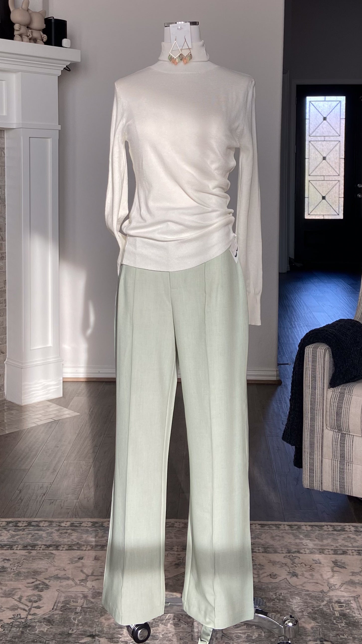 Mannequin wearing a white long-sleeve turtleneck and sage green pants in a livingroom with a fireplace