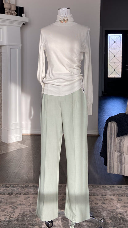 Mannequin wearing a white long-sleeve turtleneck and sage green pants in a livingroom with a fireplace