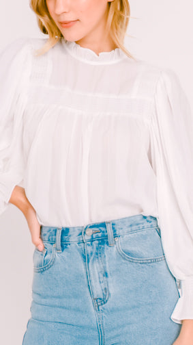 Model wearing our white Emma peasant sleeve blouse and blue jeans on a plain background